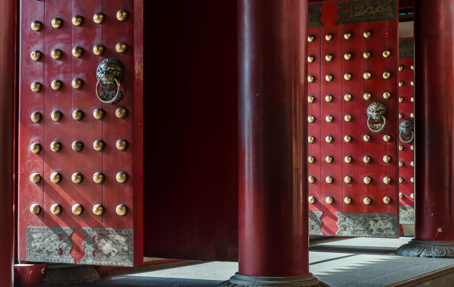 Traditional Chinese doors with brass lion head door knockers and ornamental studs. The doors are open letting in light.