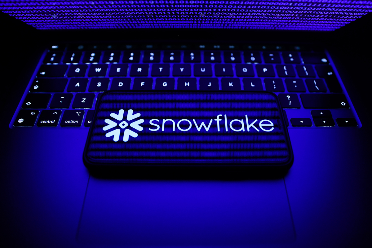 A phone showing the Snowflake logo. Phone laying on top of a laptop keyboard. 